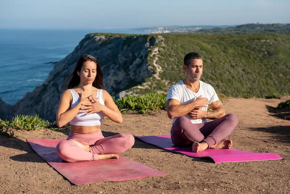 A man and woman meditating on yoga mats atop a scenic Portuguese cliff.