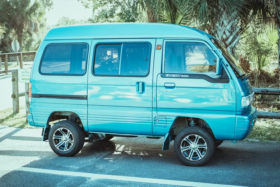 A vibrant blue minivan parked outdoors on a sunny day with lush greenery in the background.