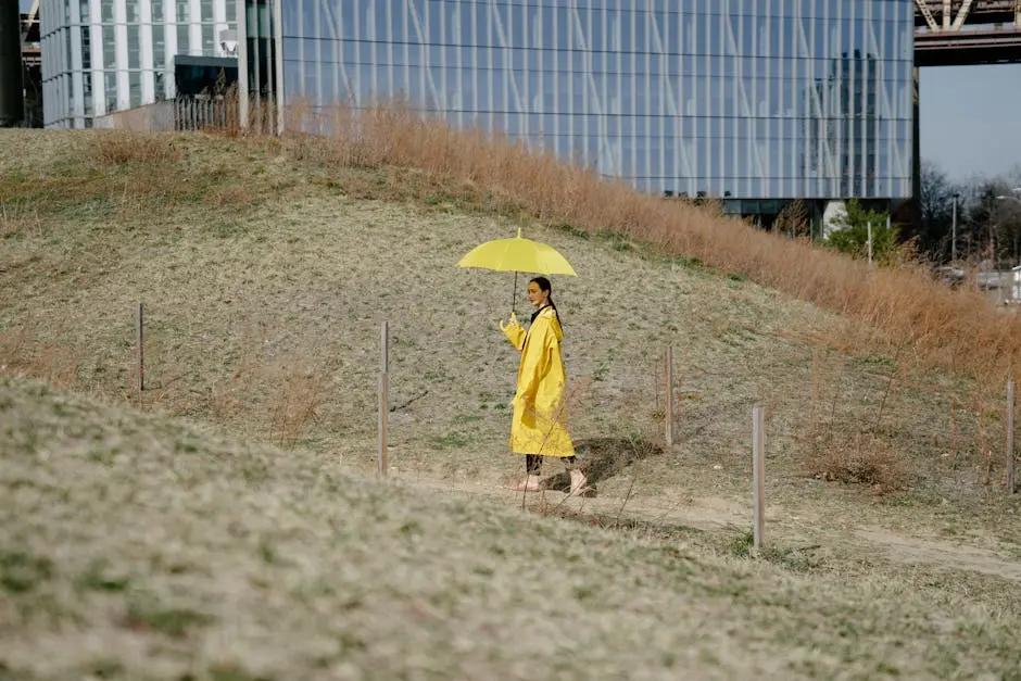 A woman in a yellow coat walks outdoors under a matching umbrella, blending fashion with nature.