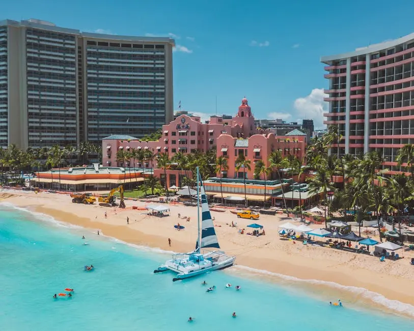 Aerial view of a vibrant beach resort with pink buildings, palm trees, and turquoise waters, highlighting leisure activities.