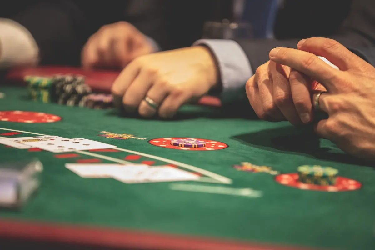 Hands playing blackjack in a casino setting with cards and chips on a green table. fractional cfo