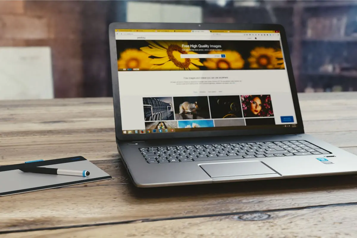 Laptop with open webpage on wooden desk, accompanied by tablet and pen, representing digital work setup.