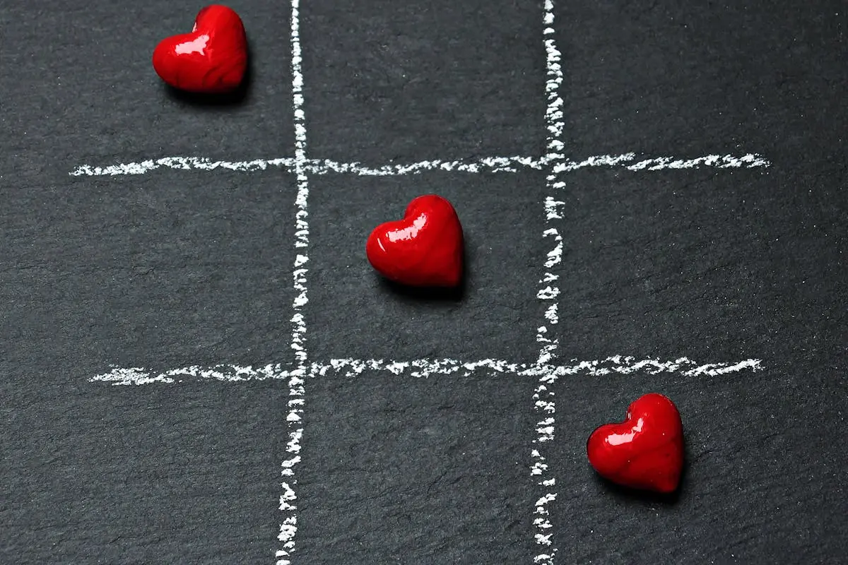 Tic tac toe board on black surface with red heart shapes symbolizing love and connection.