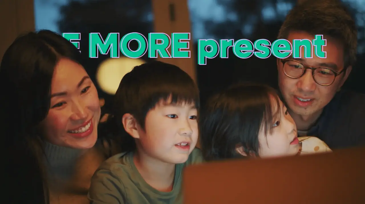 A family looking at a laptop together with the text "Be more present" animated on the screen.