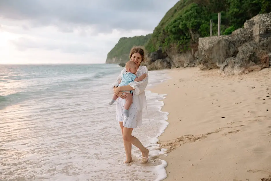 A mother carries her baby along a serene beach, enjoying the summer day.