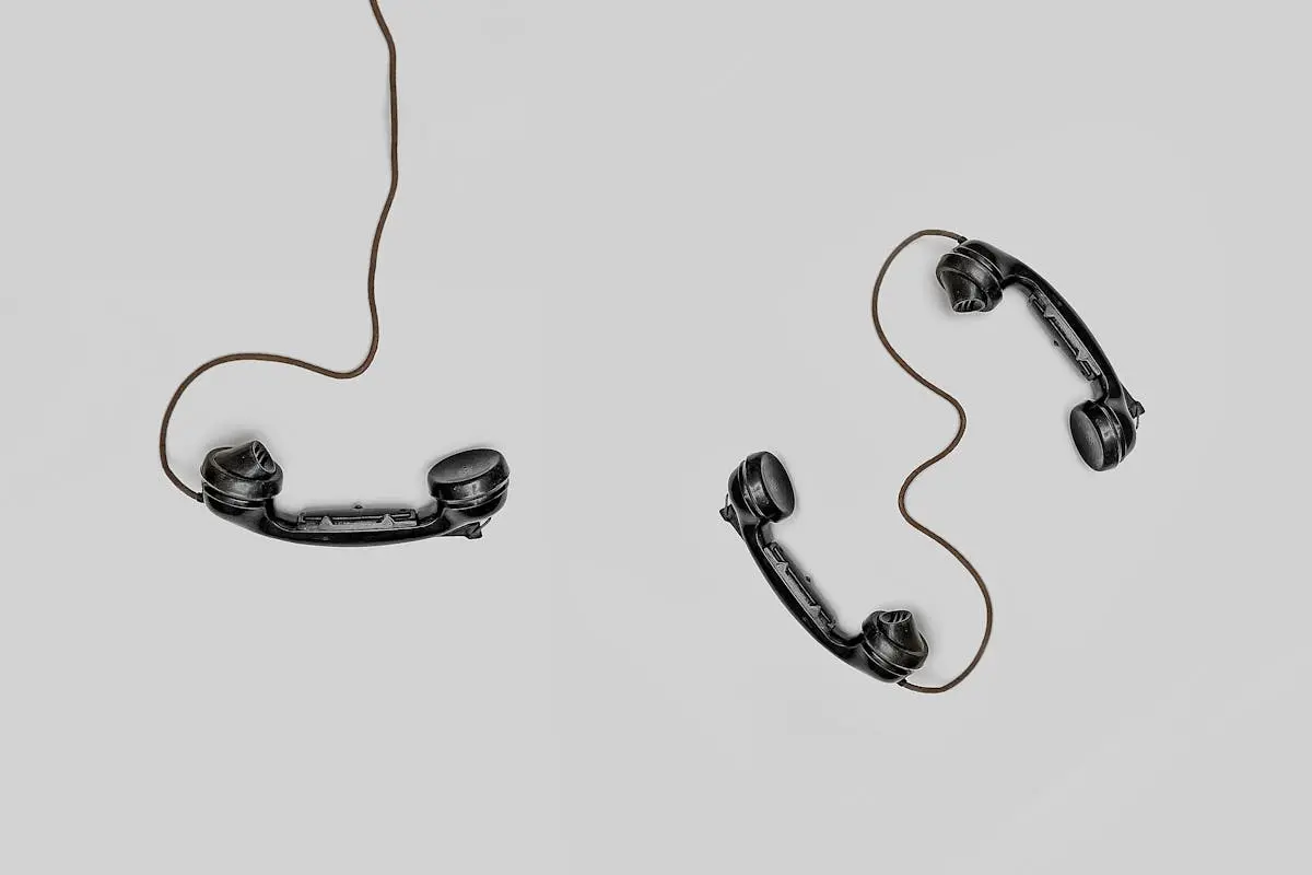 Two vintage black telephone handsets connected by cords on gray background. team leadership