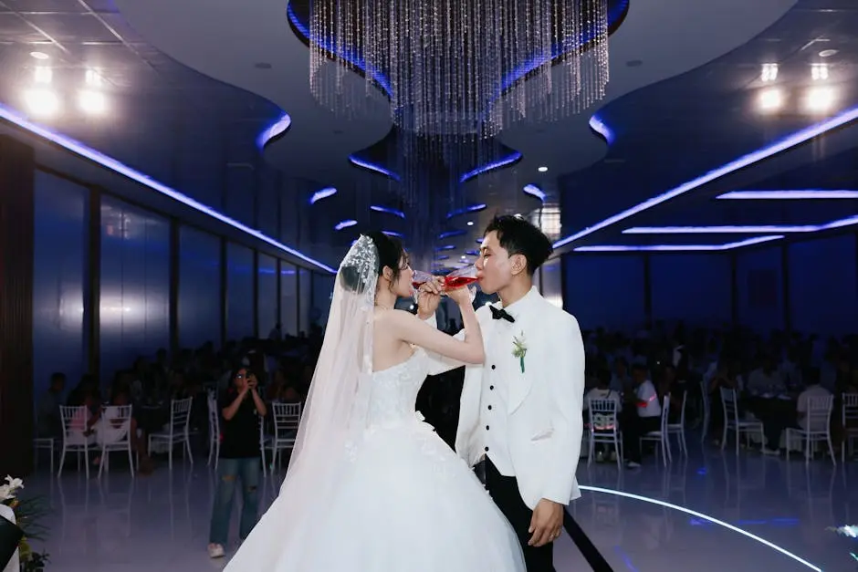 Bride and groom sharing a toast at a beautifully decorated indoor wedding ceremony.
