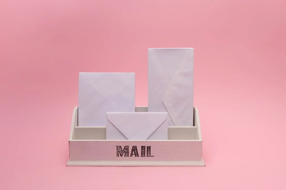 A minimalist white mail organizer with envelopes against a pink background, offering space for text.