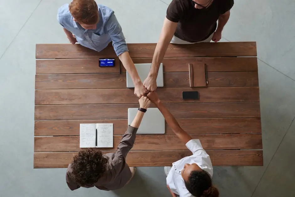 A diverse group of professionals engaging in a teamwork celebration with a fist bump over a wooden table indoors. team leadership