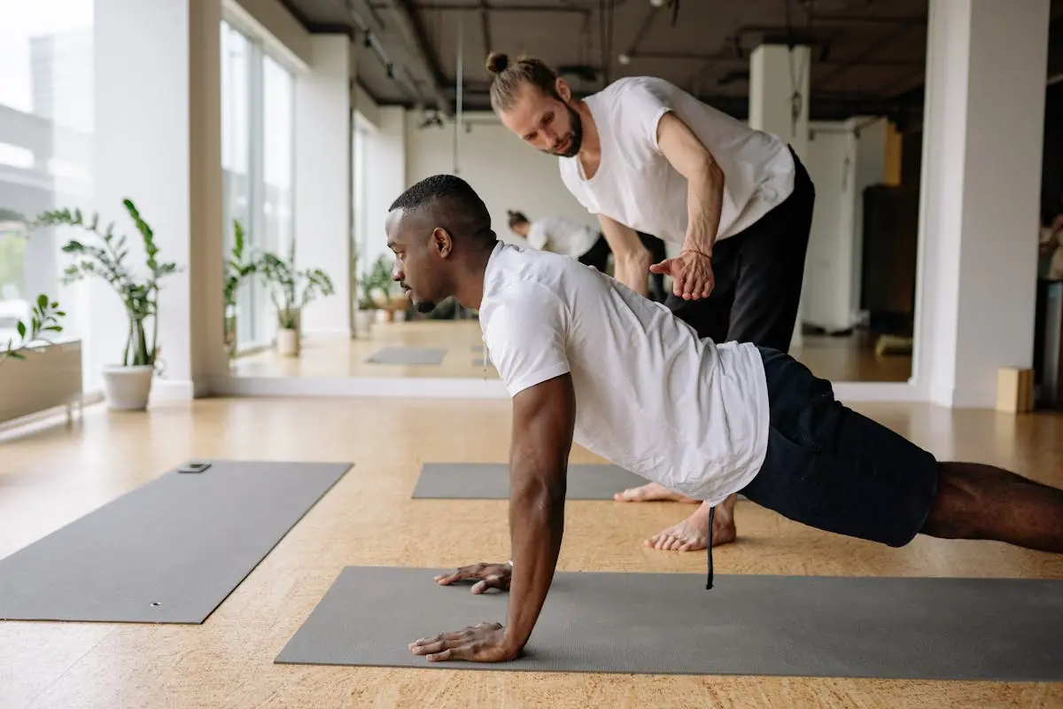A yoga instructor helps a man perfect his pose in a modern studio setting.