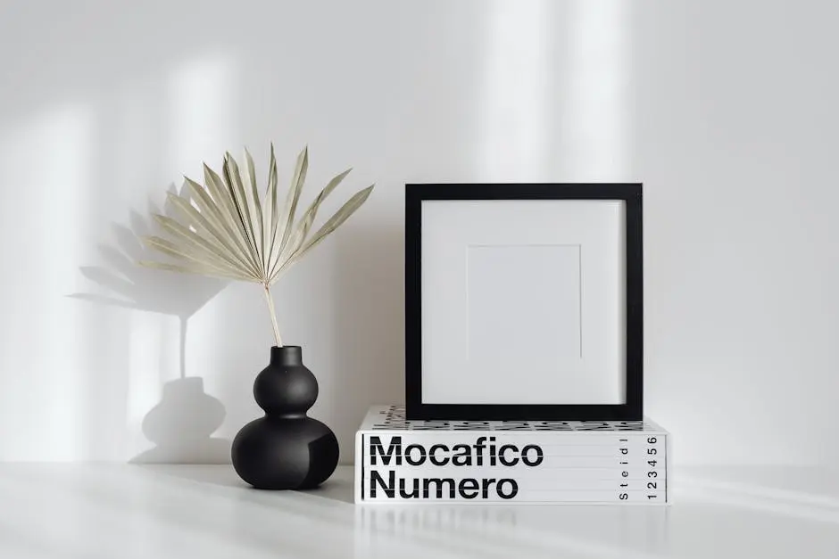 A minimalist interior setup with a black vase, leaf, and picture frame.