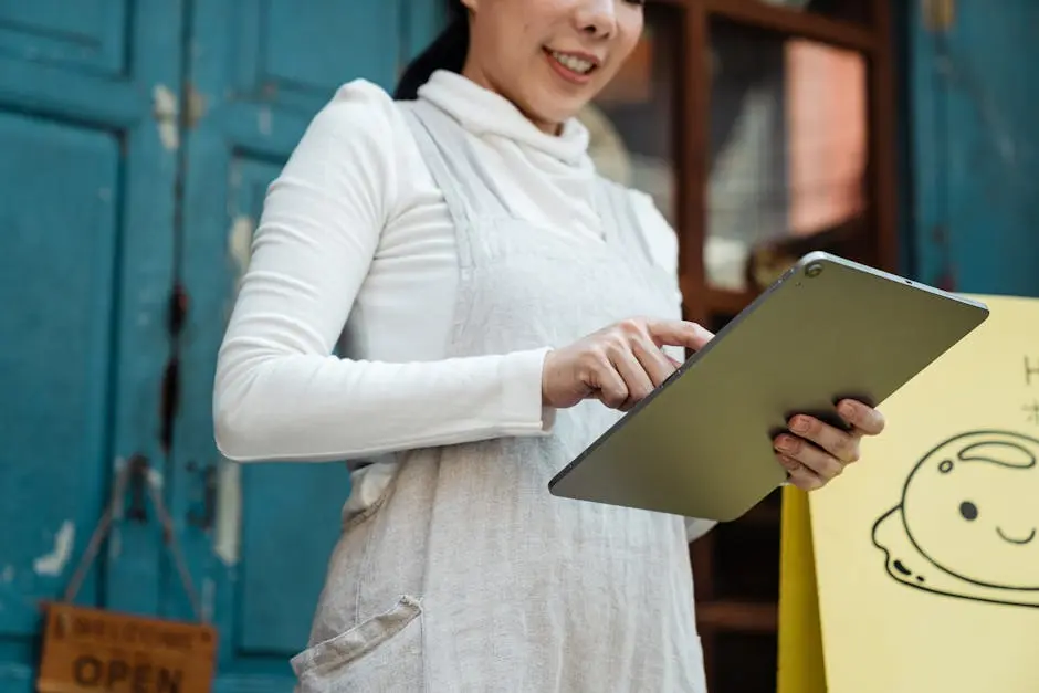 Smiling woman with a tablet in front of a shop displaying an open sign.