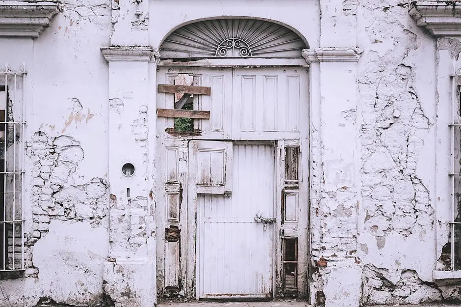 An old, decaying white building with a weathered door and cracked walls.