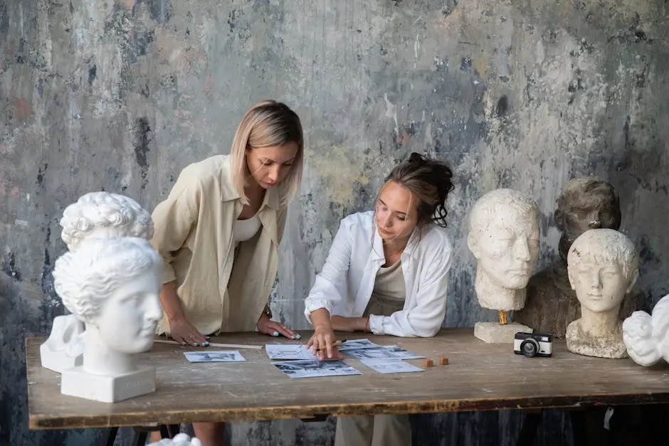 Two female artists discussing project ideas in a sculpture-filled art studio.