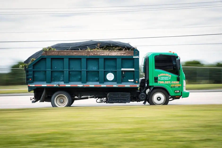 A green truck transporting yard waste on a road captured in motion. Perfect for transportation and environmental themes.