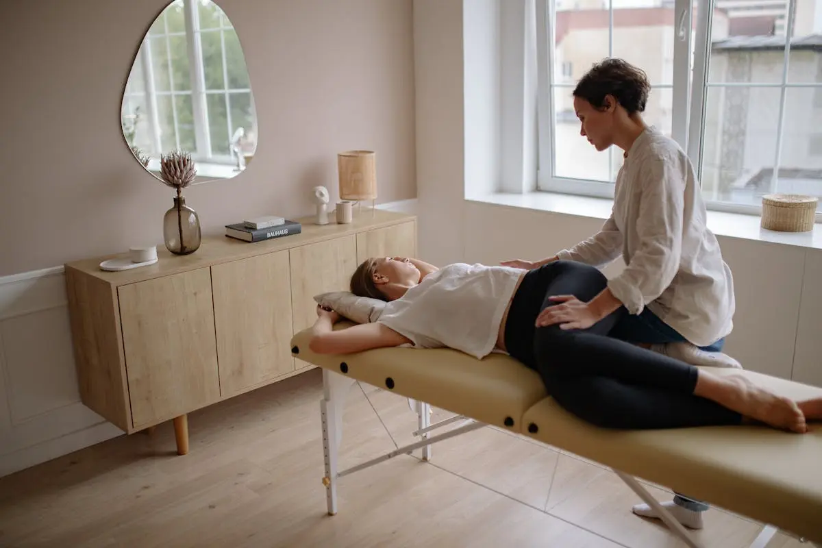 A therapist provides a calming massage to a woman lying on a massage table in a serene, well-lit room.