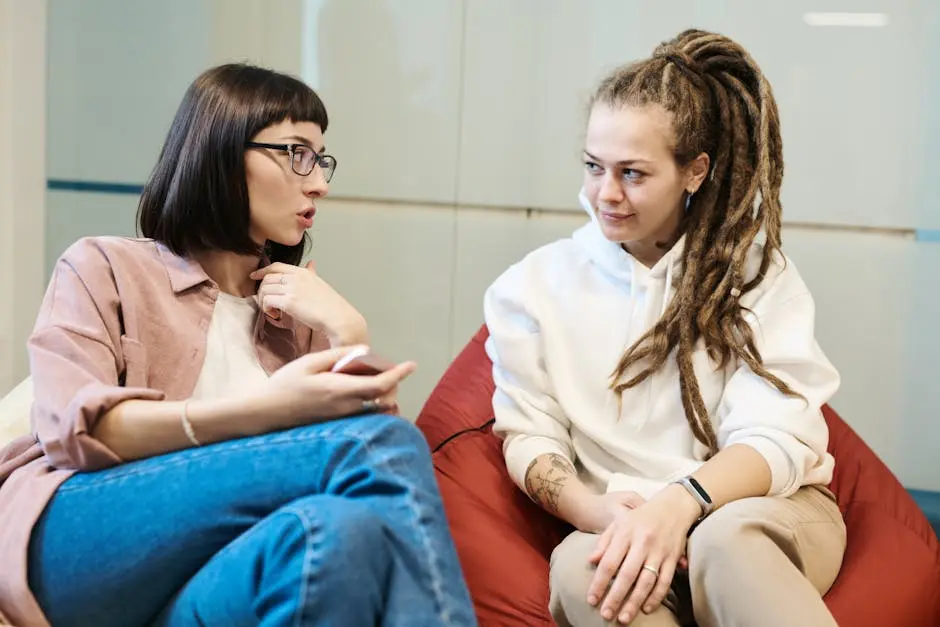 Two women engaged in a conversation in a modern office, sitting comfortably in relaxed chairs.