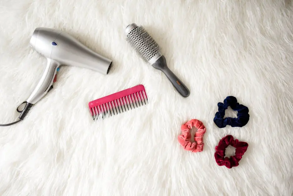 Flatlay of hairstyling tools including a hairdryer, brush, comb, and scrunchies on white fur.