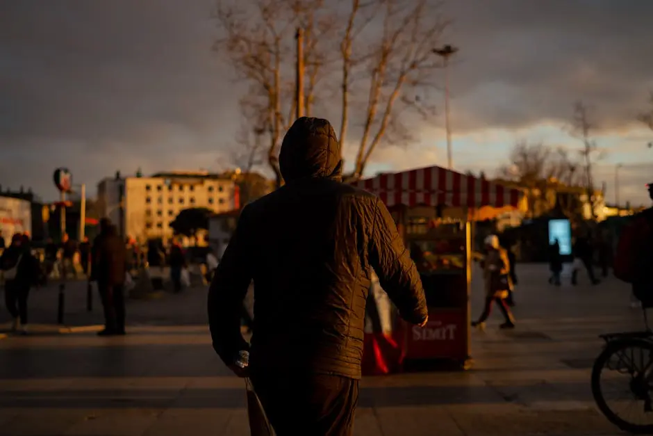 A person in a hooded jacket walks through a bustling city street at dusk.