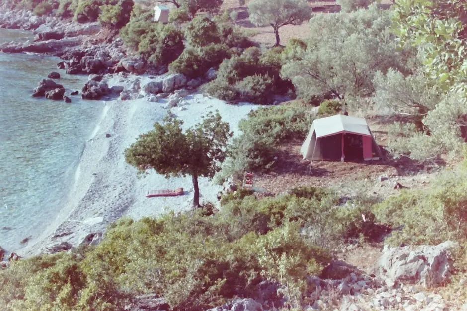 A tranquil beachfront camping site with a tent, trees, and clear sea water, perfect for a getaway.