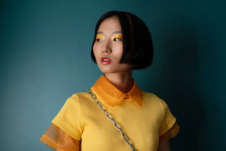 Portrait of a fashionable Asian woman with bold makeup on a teal background.