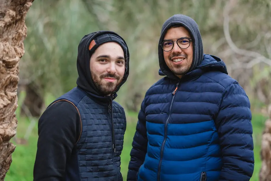 Two men warmly dressed in hooded jackets smile outdoors, showcasing winter fashion.