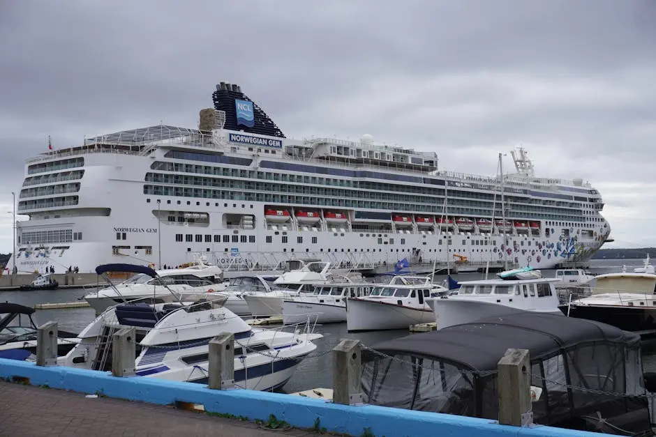 Large Norwegian Gem cruise ship docked at a harbor with smaller boats nearby.