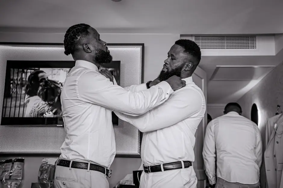 Two men adjusting their shirts in a black and white photo, reflecting professional attire and camaraderie.