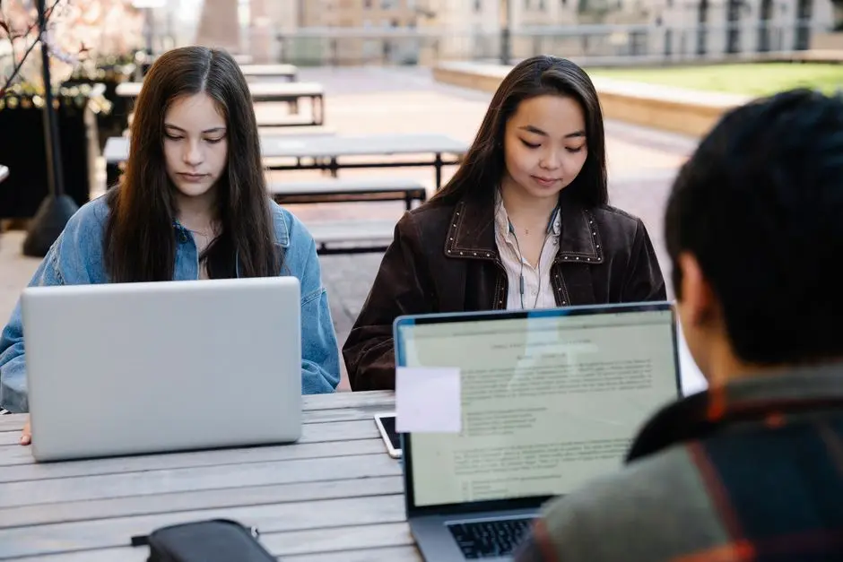 Two students focus on studying with laptops at an outdoor university setting, promoting technology and education.