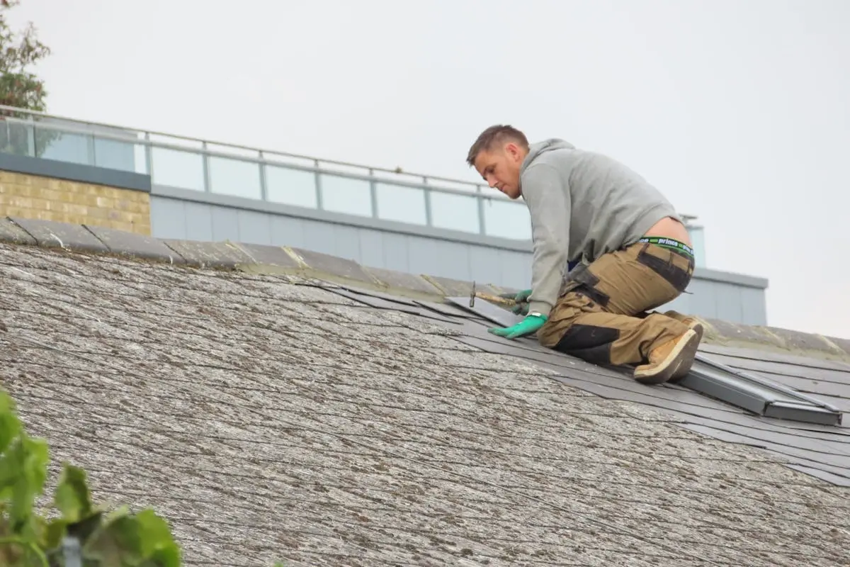 Construction worker installing shingles on a rooftop. Outdoor building maintenance.