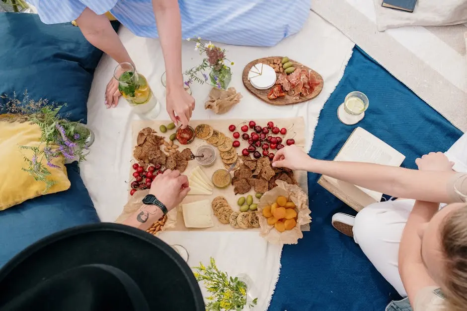 An overhead view of friends enjoying a casual summer picnic with various snacks on a blanket.
