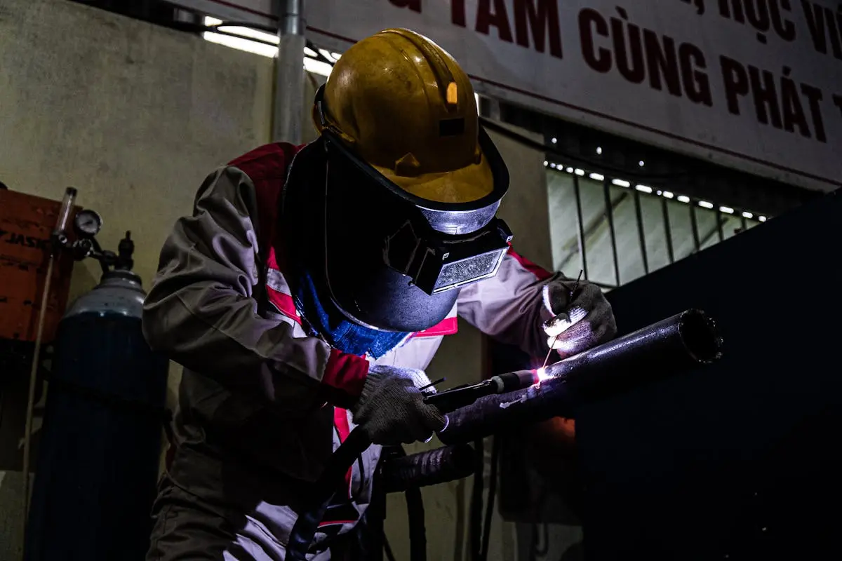 A welder skillfully working in a dimly lit industrial setting, using protective gear and equipment.
