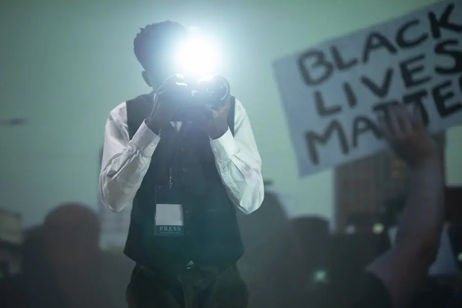 Photojournalist using camera flash at protest with Black Lives Matter sign.