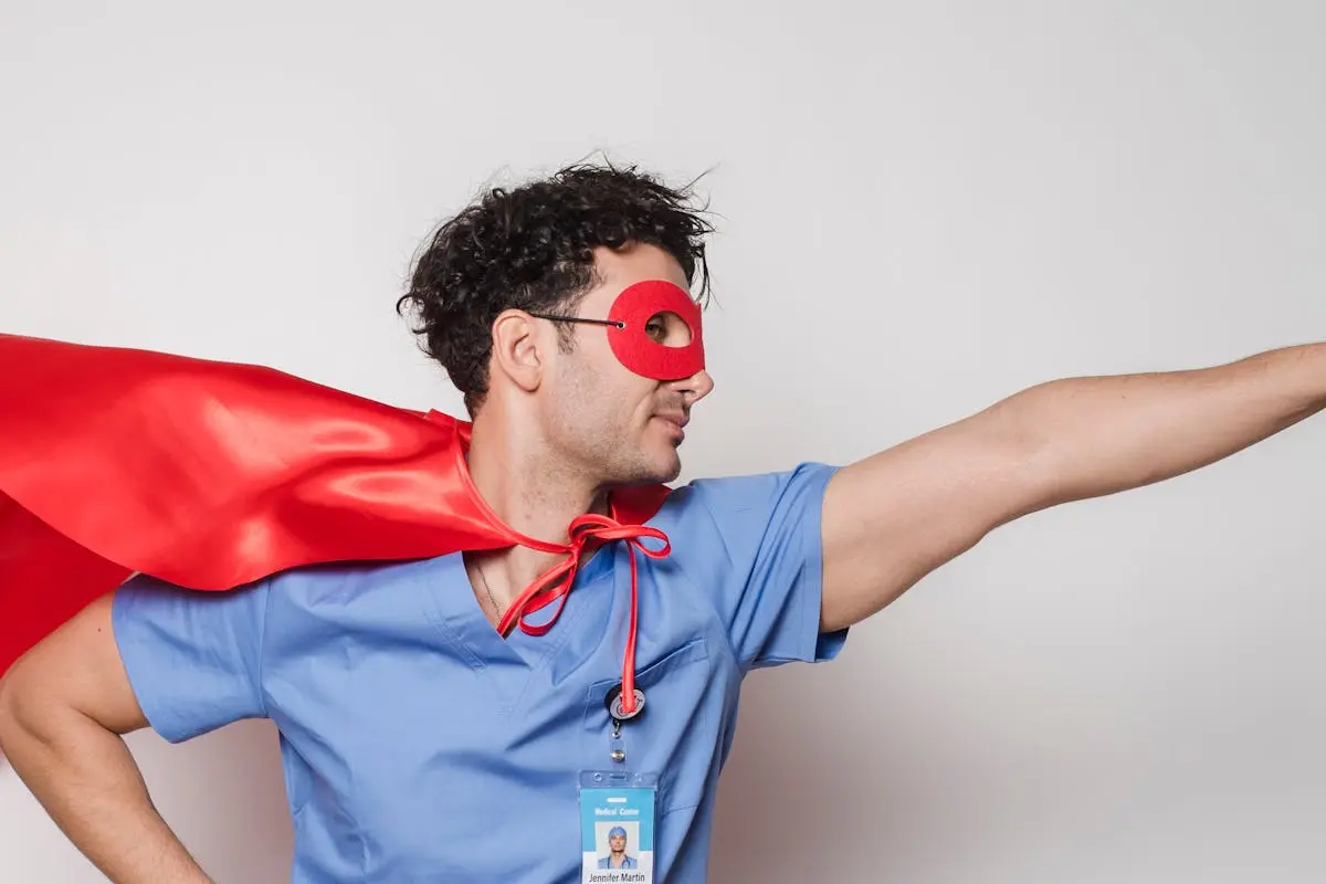 Male healthcare worker wearing a red cape and mask poses as a superhero. Studio shot.