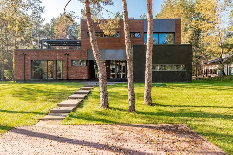 Contemporary house with large glass windows surrounded by lush greenery and a paved pathway.