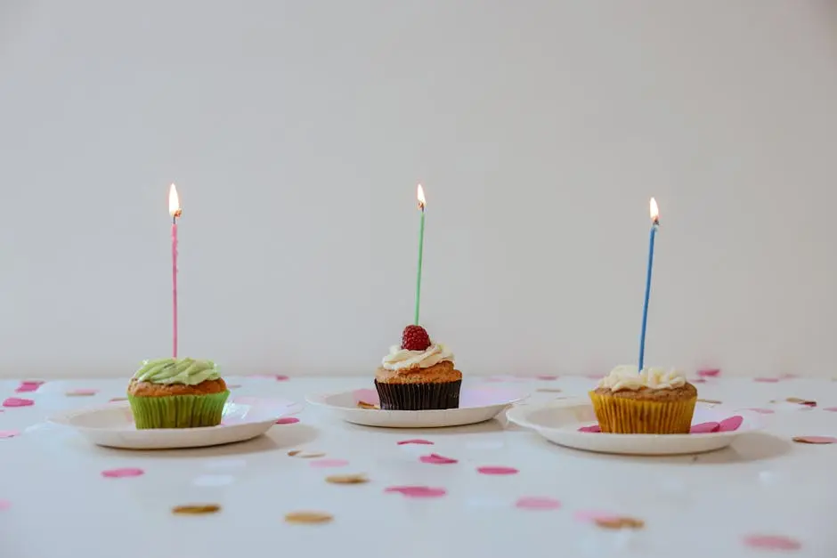 A festive arrangement of cupcakes with lit candles surrounded by confetti for a cheerful birthday celebration.