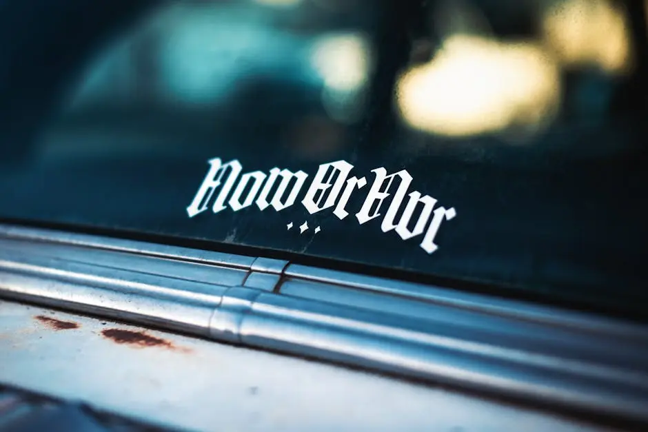 Detailed shot of a vintage car window with a unique ‘Now or Nvr’ sticker in an urban setting.