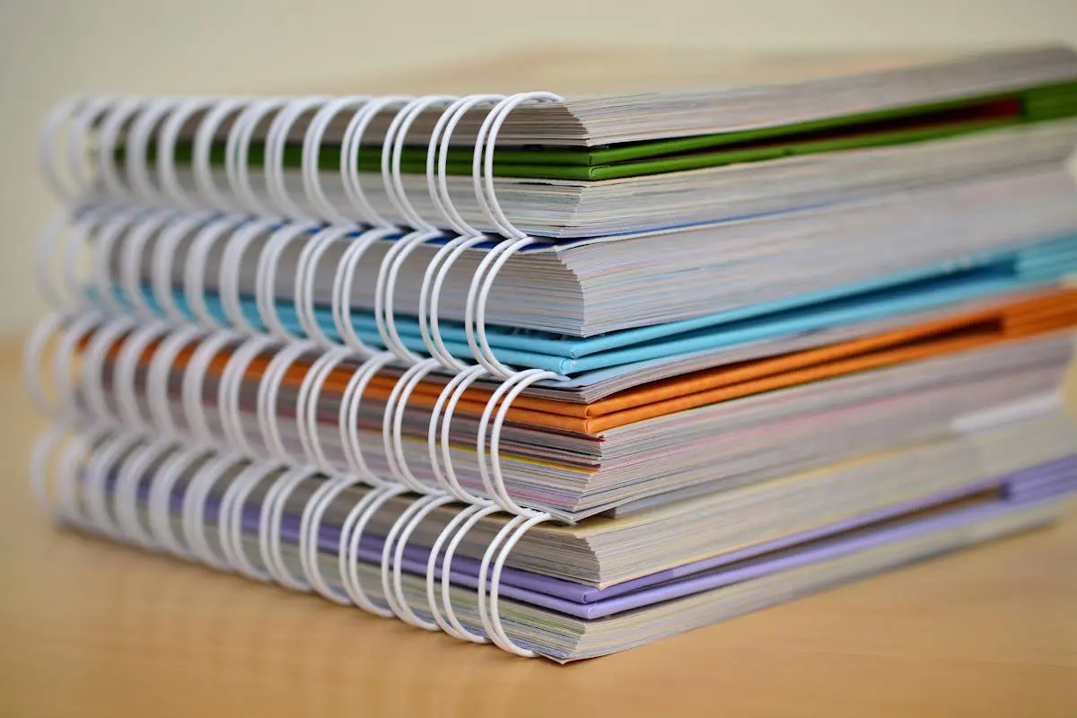 A colorful stack of spiral-bound notebooks neatly placed on a wooden desk. Ideal for growth strategy consulting