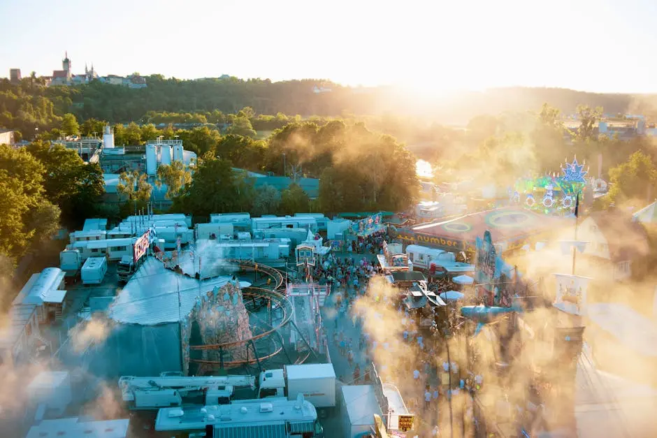 A lively amusement park captured from above during sunset, showcasing rides, crowds, and bright lighting.