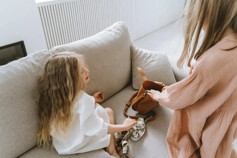 Two young girls with curly hair playfully explore a bag indoors on a cozy sofa.