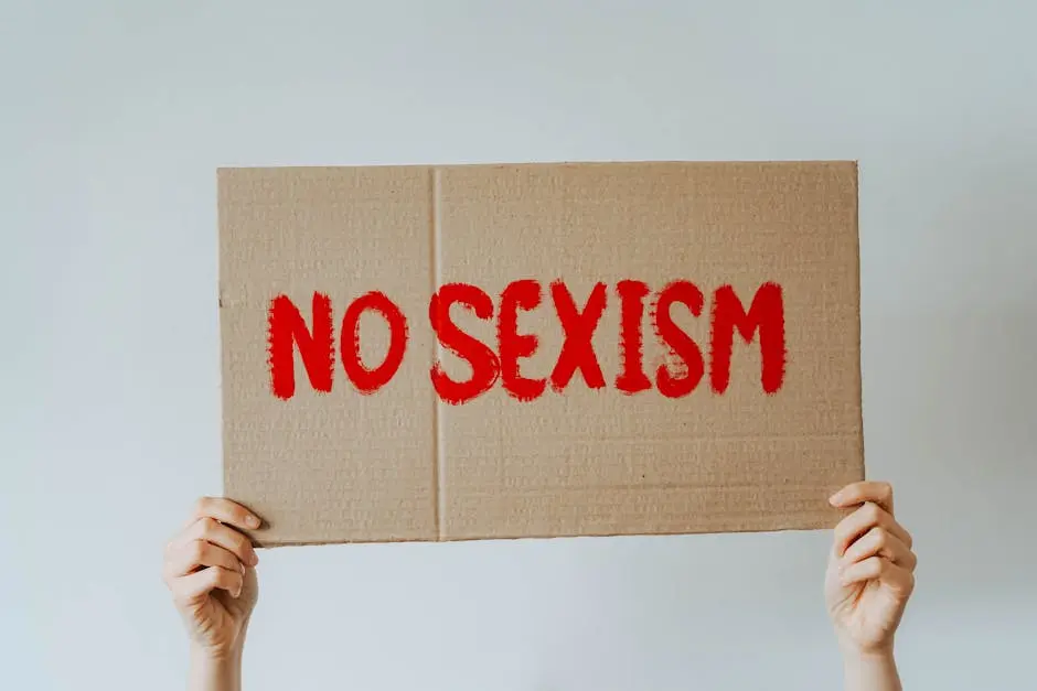 Cardboard sign held up with the message &lsquo;No Sexism&rsquo; in bold red lettering, emphasizing gender equality.