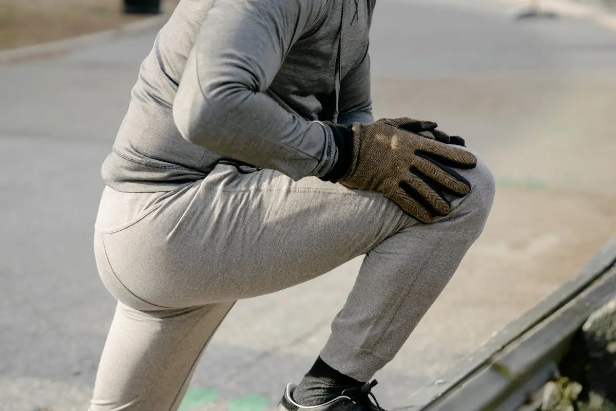 Side view of crop anonymous male athlete in sportswear stretching legs before training in city park in daylight