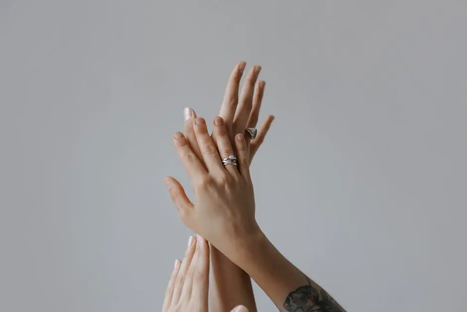 Minimalistic close-up of intertwined hands displaying rings, against a gray background. stacking rings