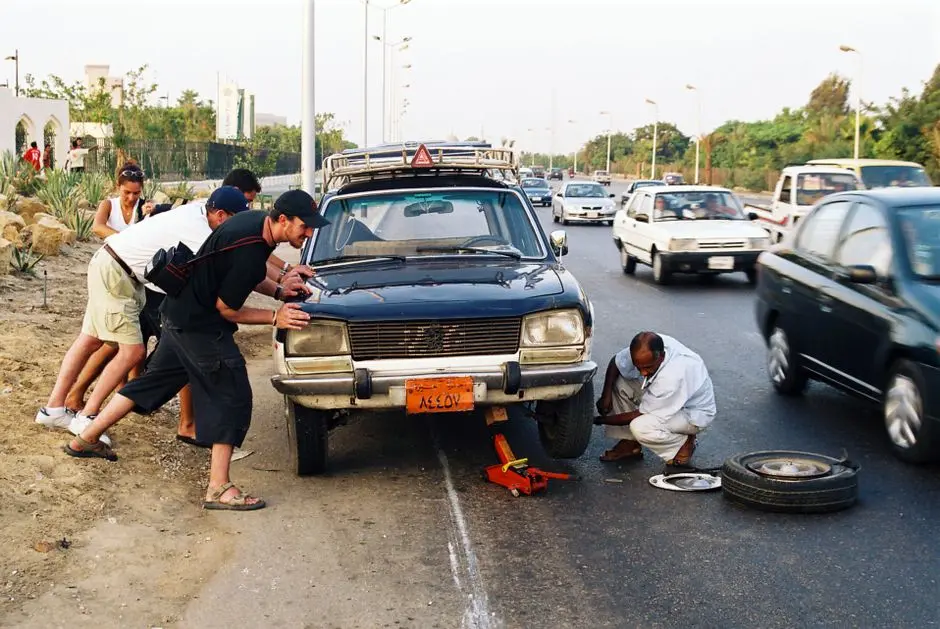 A group assists in repairing a car on a busy roadside, emphasizing teamwork and roadside assistance.