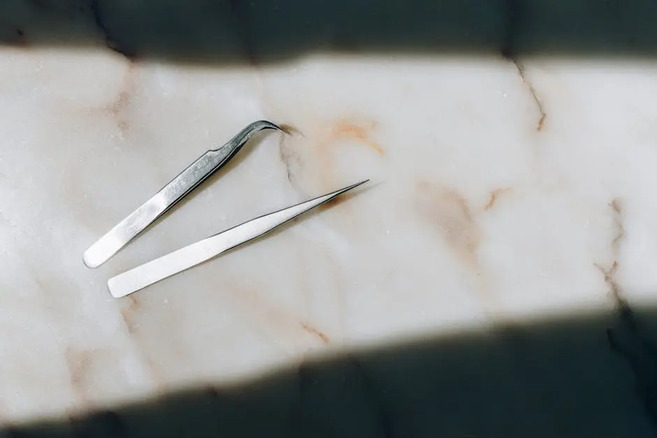 High-angle shot of two precision tweezers on a marble surface, highlighting elegance and simplicity.