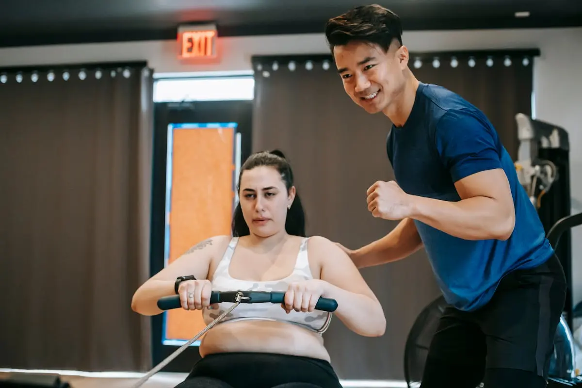 Trainer guides client on rowing machine for intense fitness session in gym.