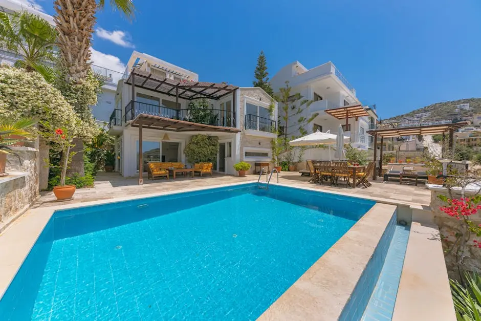 Beautiful luxury villa with a swimming pool, terrace, and lush greenery under a bright blue sky.