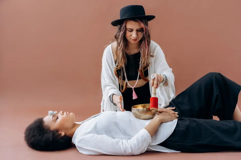 Woman practicing sound healing with singing bowl over another woman. Meditative and relaxing wellness session.