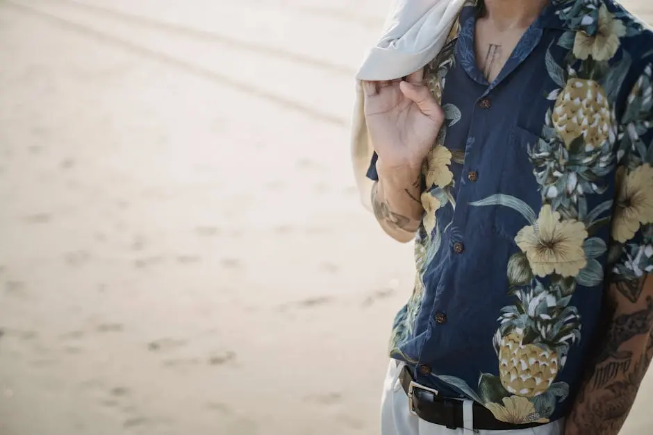 Stylish man in a tropical shirt standing on the beach, a tattoed arm holding a jacket.