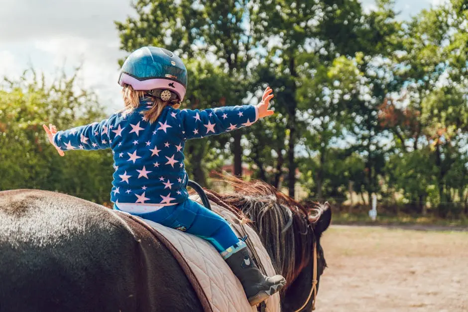 A child confidently rides a horse outdoors, wearing a helmet and star-patterned jacket.